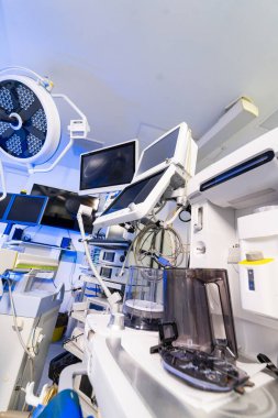Modern sinir cerrahisi ameliyathanesinde birden fazla tıbbi monitör ve ekipman var. Anestezi makinesi, monitörleri ve mavi ışıkta tıbbi cihazları olan yüksek teknoloji cerrahi süitin içi..