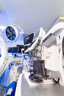 Nöroşirürji tiyatrosunda gelişmiş cerrahi ekipman ve tıbbi monitörler. Mavi ışıklandırılmış ameliyathanede ekranları, donanımı ve cerrahi ekipmanları olan tıbbi çalışma istasyonuna yakın çekim.
