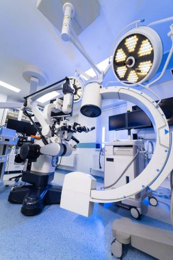 Robotik mikroskop ve C-kol ile gelişmiş sinir cerrahisi ameliyathanesi. Mavi ışıkta yüksek teknolojili nörocerrahi mikroskop ve floroskopi ekipmanlarının yer aldığı modern cerrahi tiyatro..