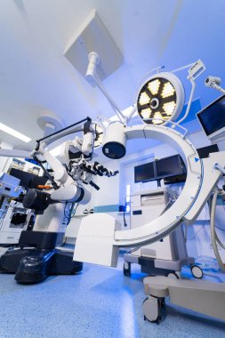 Robotik mikroskop sistemine sahip modern nörocerrahi ameliyathane. Steril nöroşirürji odasının geniş açılı görüntüsü mikroskop, monitörler ve mavi tonlarda cerrahi ışıklandırma..