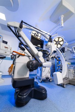 Steril ameliyathane ortamında hassas nörocerrahi mikroskop. Modern bir hastane ameliyathanesinde cerrahi lambalara karşı robotik nöroşirürji mikroskobunun düşük açılı görüntüsü.