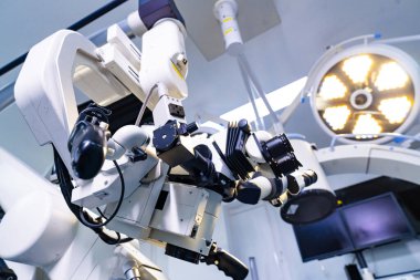 Ameliyat ışıkları altında nörocerrahi mikroskobun düşük açılı görüntüsü. Arka planda parlak dairesel cerrahi lambalar ile aşağıdan görünen optik cerrahi sistem.