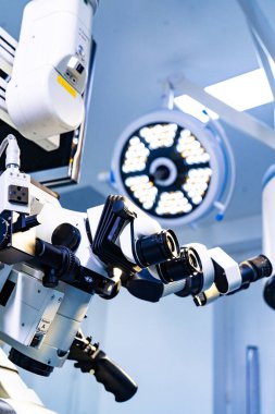 Tıbbi mikroskobun optik göz kapakları ve cerrahi ışıklandırma. Arkaplanda parlak dairesel ışık olan cerrahi mikroskobu kapat.