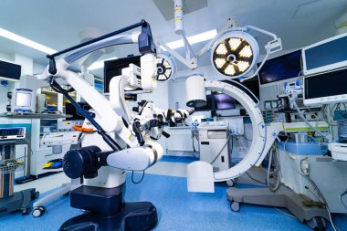 Ameliyat odasında gelişmiş nörocerrahi mikroskop ve C-kol röntgeni. Hastanedeki mobil bir C-kolu floroskopi sisteminin yanına yerleştirilmiş robotik cerrahi mikroskobun yan görüntüsü.