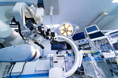 Cerrahi mikroskop ve mobil C-kol görüntüleme sistemi nöroşirürji odasında. Arka planda C-kolu floroskop ve tıbbi monitörlerle nöroşirürji mikroskobunun profil görüntüsü.