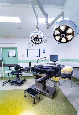 Ameliyat masası ve LED ışıkları olan modern ameliyathane. İçinde siyah ayarlanabilir masa, tıbbi lambalar ve kireç yeşili döşeme bulunan boş cerrahi tiyatronun içi.