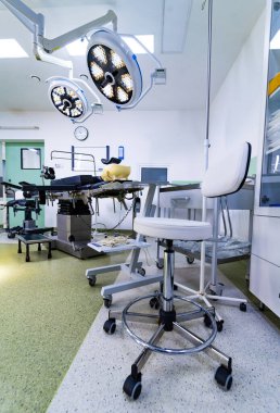 Ayarlanabilir sandalye ve ekipmanlarla modern bir ameliyathane. Beyaz tekerlekli sandalye, ameliyat masası ve yukarıdaki lambalar da dahil olmak üzere hastane ameliyathanesi manzarası..