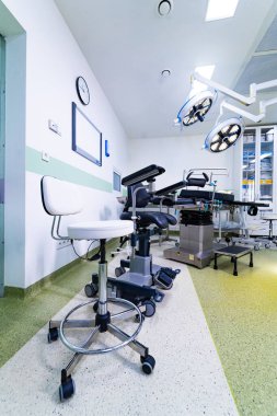 Ameliyat masası ve tıbbi koltuğu olan bir ameliyathane. Profesyonel cerrahi masası, taburesi ve ışıklandırma ekipmanlarının yer aldığı steril tıp odasının ayrıntılı görüntüsü.