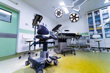 Hastane ameliyathanesinde profesyonel masa ve ışıklandırma var. Cerrahi masası, tıbbi tabure, dolaplar ve tavan lambalar ile işlevsel tıbbi iç mekan.