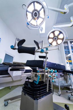 Bacak destekli ameliyat masasının düşük açılı görüntüsü. Parlak LED lambaların altında ayarlanabilir tıbbi üzengi ve ameliyat masasının ayrıntıları.