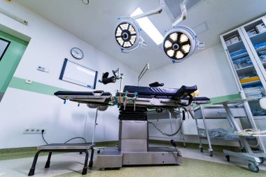 Ameliyathanede ayarlanabilir ameliyat masasını kapatın. Tıbbi ekipman ve ışıklarla ayarlanabilir siyah ameliyat masasının detaylı görüntüsü.