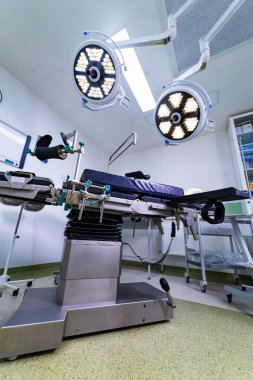 Ameliyat masası ve lambaları olan modern ameliyathane. Parlak ameliyat ışıkları altında ayarlanabilir bir ameliyat masasının bulunduğu steril bir tıbbi tiyatronun içinde..