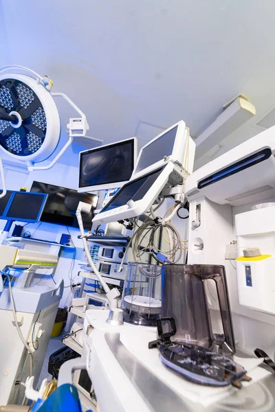 Modern sinir cerrahisi ameliyathanesinde birden fazla tıbbi monitör ve ekipman var. Anestezi makinesi, monitörleri ve mavi ışıkta tıbbi cihazları olan yüksek teknoloji cerrahi süitin içi..