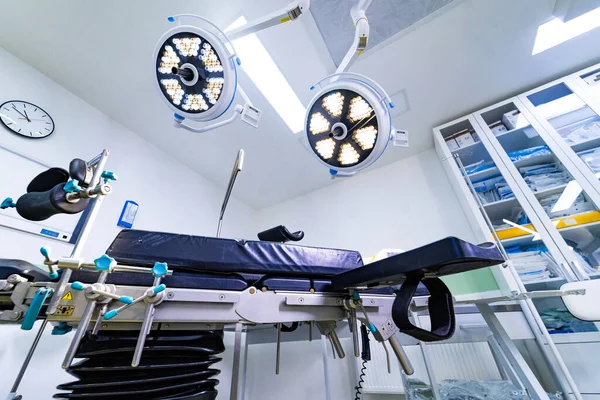 Steril hastane odasındaki ayarlanabilir ameliyat masasını kapatın. Parlak bir klinik ortamında bacak destekleri ve tıbbi dolapları olan mekanik bir ameliyat masasının ayrıntılı görüntüsü.