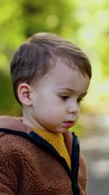 Dışarıda oynayan tatlı, beyaz bir çocuk. Bebek kestane fırlatır ve almak için koşar. Arka planda bulanık doğa. Dikey video