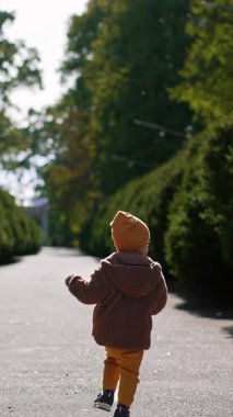 Parkın arka sokağında koşan çocuğun görüntüsü. Güneşli bir sonbahar gününde açık havada zaman geçirmek. Dikey video