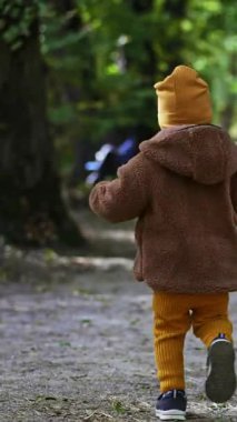 Parktaki sokakta koşan küçük, aktif bir çocuğu takip ediyorum. Doğada gezen küçük bir çocuk. Dikey video