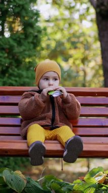 Güzel, beyaz bir çocuk doyma paketinden meyve püresi yiyor. Parkta yürürken sağlıklı atıştırmalıklar. Dikey video