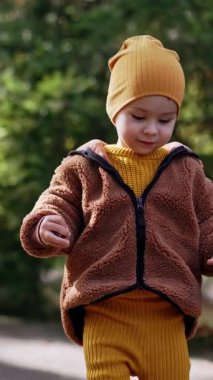 Güzel beyaz çocuk yerden kestane topluyor. Yavru sonbaharda dışarıda eğleniyor. Dikey video