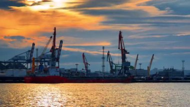 Burgas, Bulgaria, 29 June 2025: Huge empty container ship stands in the port waiting for loading. Numerous cargo handling equipment at backdrop. View from the waterscape colored orange at sunset time.
