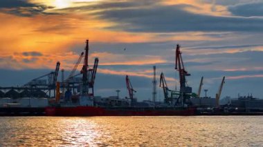 Burgaz, Bulgaristan, 29 Haziran 2025: Limanda turuncu ve mavi bulutlu gökyüzüne karşı çok sayıda kargo taşıma ekipmanı kaldırıldı. Kıyıda boş yük gemisi duruyor. Gün batımında su manzarasından rıhtıma bak..