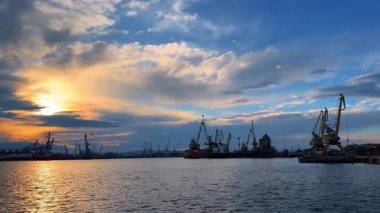 Limanda yüklü yükleme ekipmanları var. Gün batımında rıhtımda yük taşımak için konteyner vinçleri. Sudan bakış açısı.