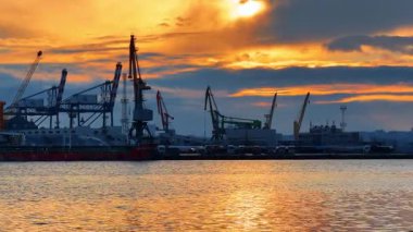Burgaz, Bulgaristan, 29 Haziran 2025: Gün batımında mavi-turuncu gökyüzüne karşı liman makineleri. Kargo gemisi, birden fazla kamyon ve konteynır vinci rıhtımda..
