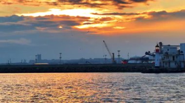 Deniz feneri, kuleler, limanda vinç patlamaları. Gün batımında su manzarasından alçak açılı rıhtım manzarası.