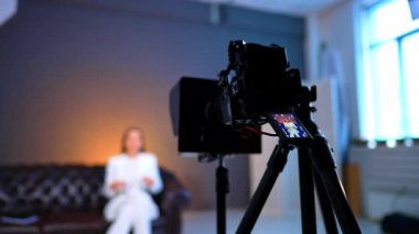 Modern kamera, bulanık arkaplanda beyaz takım elbiseli bir kadını kaydediyor. Kapatın. Blog görüntüleri sahne arkasında.