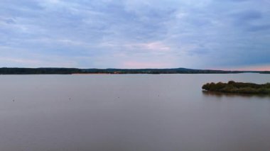 Altmuhlsee Gölü 'nün geniş manzarası bulutlu günbatımı gökyüzünün altında. Sakin göl su yüzeyi, küçük adalar ve bulutlu gece gökyüzü altında uzak kıyı şeridi pembe günbatımı parlaklığında..