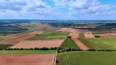 Almanya 'daki tarımsal tarlalara ve kırsal alanlara dair hava görüşü. Yazın mavi bulutlu gökyüzünün altında geniş tarımsal tarlalar, yeşil çayırlar ve küçük bir köy..