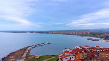 Kıyı koyunda küçük bir rıhtım ve konut binaları var. Deniz koyunun havadan görünüşü, kayıklı taş iskele, ve kıyıda modern binalar..