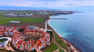 Deniz feneri olan bir sahil beldesinin panoramik manzarası. Dairesel konut kompleksinin geniş hava manzarası ve turkuaz deniz kıyısı boyunca bir deniz feneri.