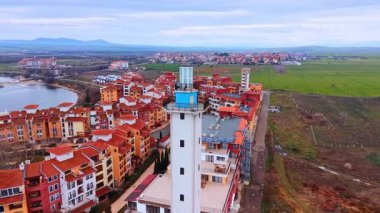 Deniz feneri kulesi ve yerleşim bölgesi hava manzarası. Arka planda kırmızı çatılı yerleşim alanı olan beyaz bir deniz feneri kulesine odaklanmış yüksek açılı çekim..
