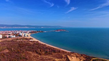 Kumlu sahili ve uzak kasabası olan kıyı manzarası. Eğri kumlu bir sahil, orman alanı ve uzak bir sahil kasabasının geniş hava manzarası..