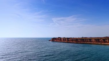 Sakin deniz suyuna bakan doğal kayalık kıyı şeridi. Dikey bir kıyı uçurumu ve kayalık kıyıların derin mavi okyanus suyuyla buluşmasının yüksek açılı görüntüsü.