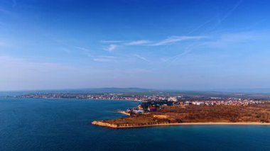 Kıyı şeridi ve kumsalın geniş hava manzarası. Açık gökyüzünün altında mavi denize uzanan küçük yarımadası olan uzun kumlu bir sahil şeridinin panoramik manzarası.