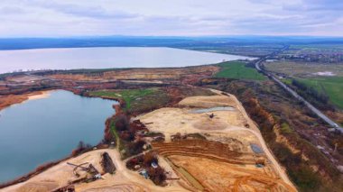 Kum ocağı ve büyük gölün panoramik manzarası. Geniş açı, geniş bir göl ve yeşil alanların yanında bir kum madenciliği operasyonunun ölçeğini gösteriyor..