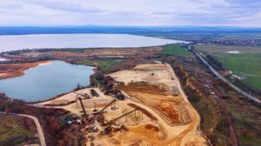 Kum çıkarma ve gölün havadan panoramik görüntüsü. Büyük bir göle bitişik ekipman, taşıyıcılar ve stoklarla geniş bir kum ocağı görüntüsü..