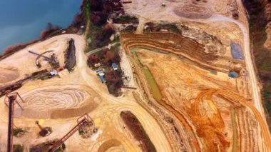 Suyun yakınındaki kum ocağının geniş açılı hava görüntüsü. Makineler, stoklar ve büyük bir su kütlesi ile aktif bir kum çıkarma alanının panoramik görüntüsü.