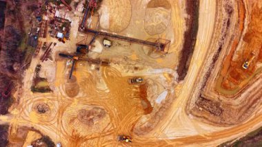 Taş ocağında endüstriyel makineler ve taşıyıcılar var. Taş ocağı altyapısının dikey aşağı görüntüsü, taşıma bantları, tekerlek yükleyicileri, ve kumdaki lastik izleri..