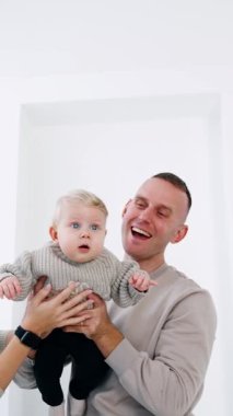 Gülümseyen beyaz bir çift kucağında küçük bir bebek taşıyor. Ebeveynler küçük oğullarına el sallıyor. Beyaz zemin. Dikey video