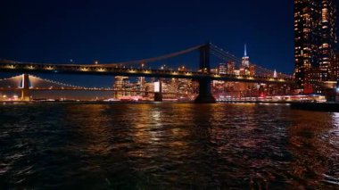 Manhattan ve Brooklyn Köprüleri gece aydınlandı. Arka planda şehrin ufuk çizgisi olan iki aydınlatma köprüsünün gece görüntüsü.