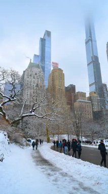 New York, ABD, 9 Şubat 2026, Central Park 'ta sisli gökdelenlerle kaplı karlı bir yol. Central Park 'ta kış patikasında yürüyen insanlar yüksek binaların tepelerini sislerle kaplıyor..