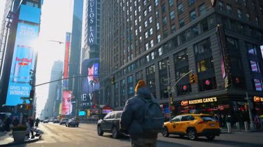 New York, ABD, 5 Ekim 2025: Sunny Times Meydanı sokak manzaralı sarı taksi. Sarı bir taksi, yayalar ve güneş ışığında büyük dijital reklam panolarının yer aldığı geniş açılı kentsel sokak manzarası.