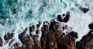 Karanlık kıyı kayalarında okyanus dalgaları kırılıyor. Yüksek açılı beyaz sörf sahili fotokopi alanı ile kayalık kıyıya vuruyor.