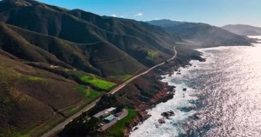 Pasifik Sahil Otoyolu 'nun havadan görünüşü Big Sur kıyı şeridi boyunca dönüyor. Sahil yolu açık mavi gökyüzünün altında yeşil dağlar ve okyanus arasında