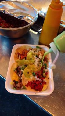 Taze tacolara limon sıkmak ve sos eklemek. Yeşil salsa sosu dökülüyor ve tepside takoların üzerine limon sıkılıyor..