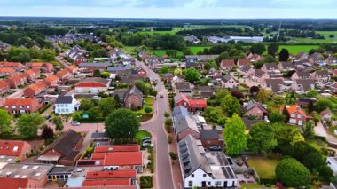 Hollanda 'nın varoşlarındaki bir T kavşağının havadan görünüşü. Kırmızı çatılı evler, yeşil ağaçlar ve park halindeki özel arabalarla çevrili bir yol kavşağının net bir görüntüsü..