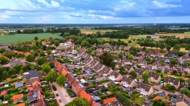 Yeşil tarlaların yakınındaki bir Hollanda kasabasının geniş hava manzarası. Bulutlu bir gökyüzünün altında geniş yeşil tarımsal alanlara dönüşen yerleşim yeri manzarası.